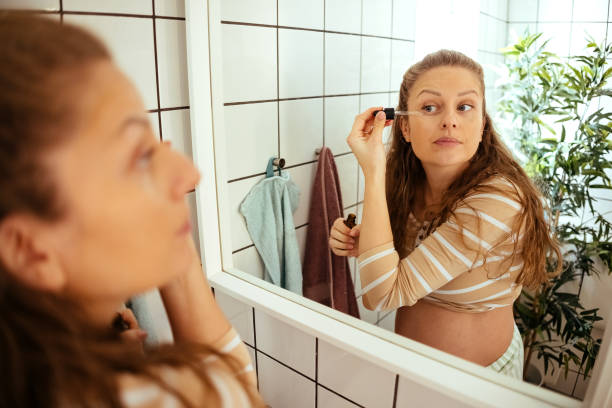 Expectant mother applying makeup in bathroom mirror