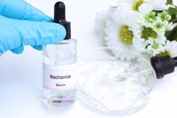 A gloved hand holding a dropper above a small bottle labeled Niacinamide Serum next to white and green