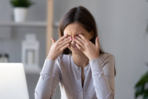 Woman feeling stressed and covering her eyes while sitting at a desk with a laptop