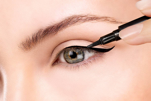 Close-up of a person applying black eyeliner to upper eyelid